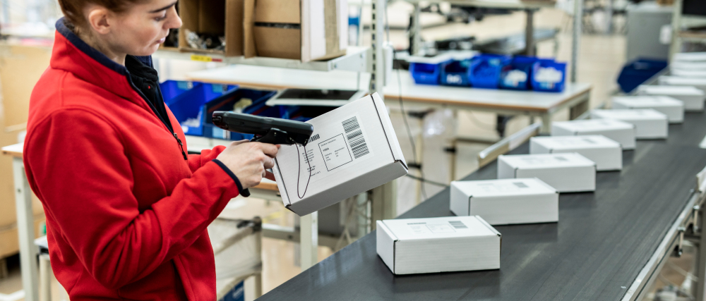 Das Bild zeigt eine Frau in einer Produktionsstraße, die im Kontext der Real-time Visibility ein Paket mittels Barcode abscannt.