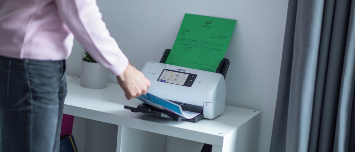 Eine Person, die vor einem Scanner steht und ein gescanntes Dokument herausnimmt.