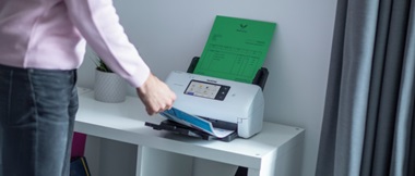 Eine Person, die vor einem Scanner steht und ein gescanntes Dokument herausnimmt.
