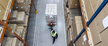 Ein Lagermitarbeiter, der einen Hubwagen mit verpackten und etikettierten Brother-Geräten in einem Lagerhaus zieht.