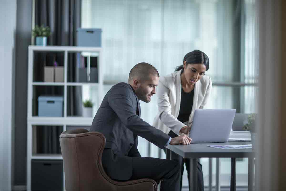 Eine Dame und ein Herr sitzen an einem Tisch und schauen auf einen Laptop.