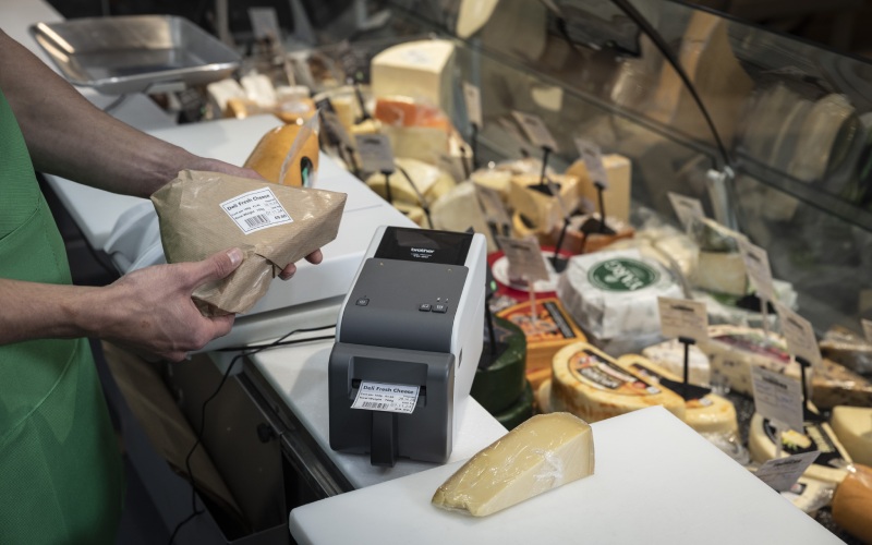 Es wird ein verpacktes Stück Käse mit einem trägerlosen Etikett beklebt.