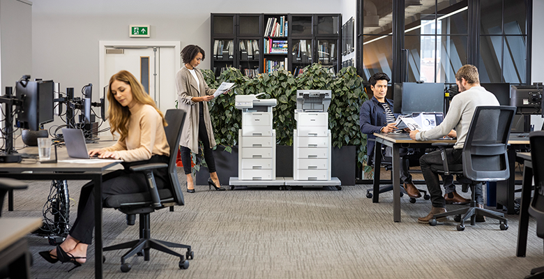 Personen sitzen einem Büro. Zwei Brother Drucker im Hintergrund.