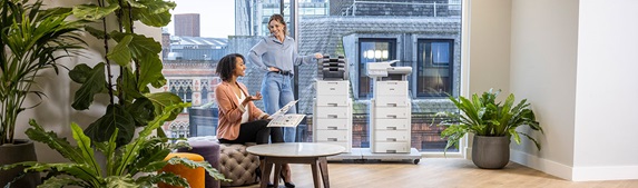 Zwei Frauen in einem großen Büro, zwei Brother-Drucker, Pflanzen, Fenster, Tisch