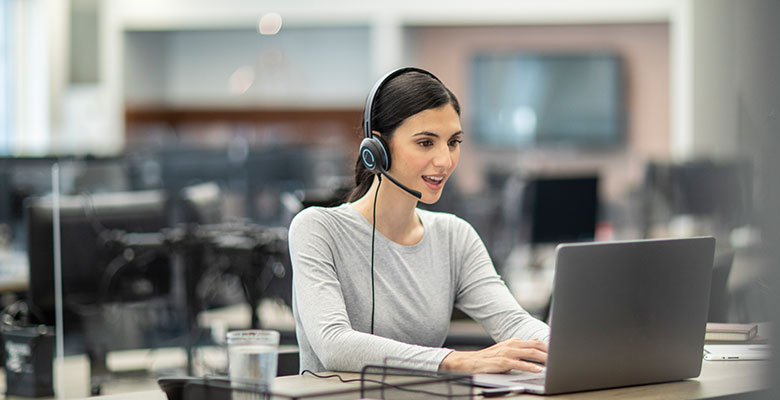 Frau mit Headset arbeitet am Laptop in einem großen Büro